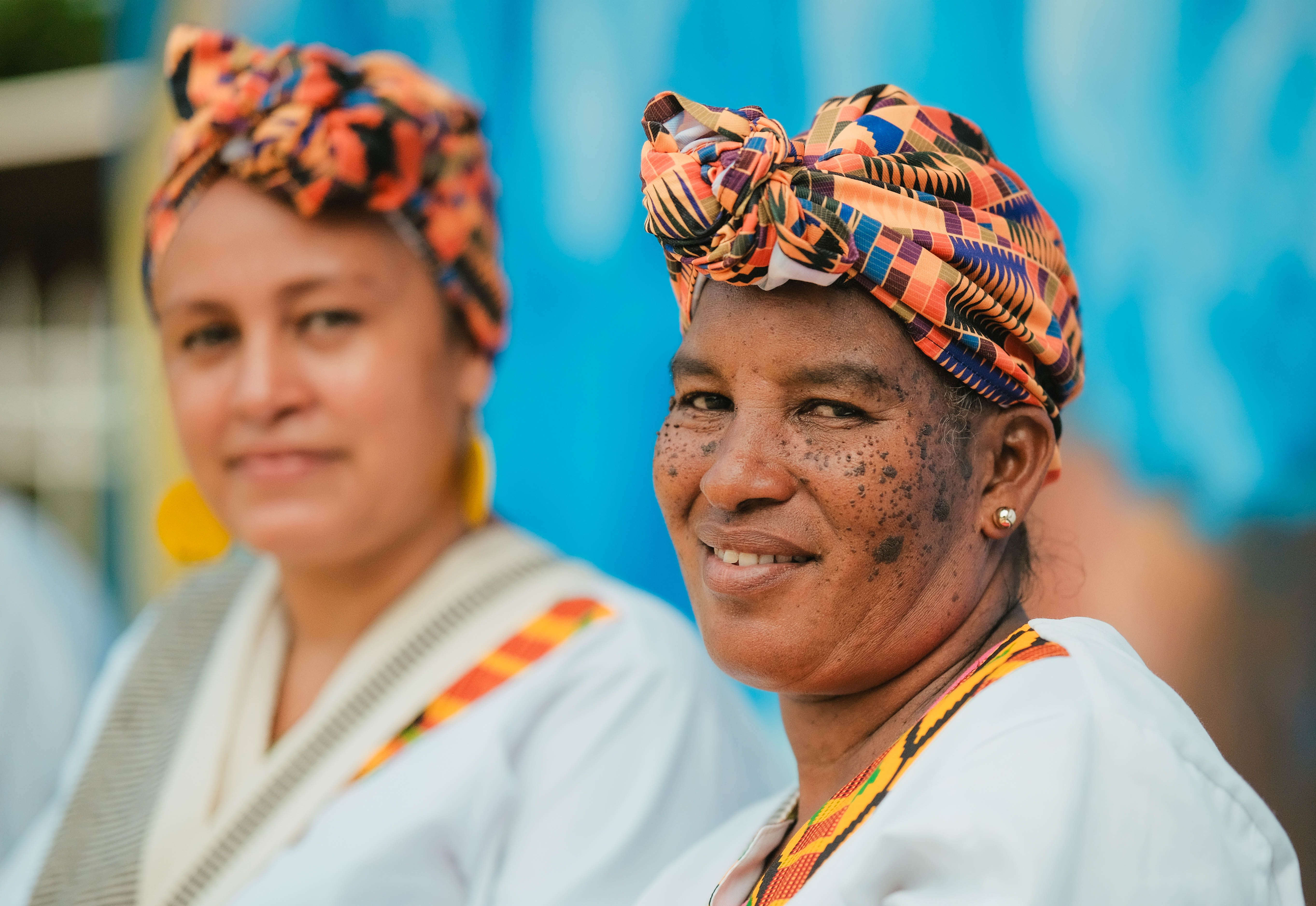 Imagen de dos mujeres adultas sonriendo. Ambas usan turbantes de colores.